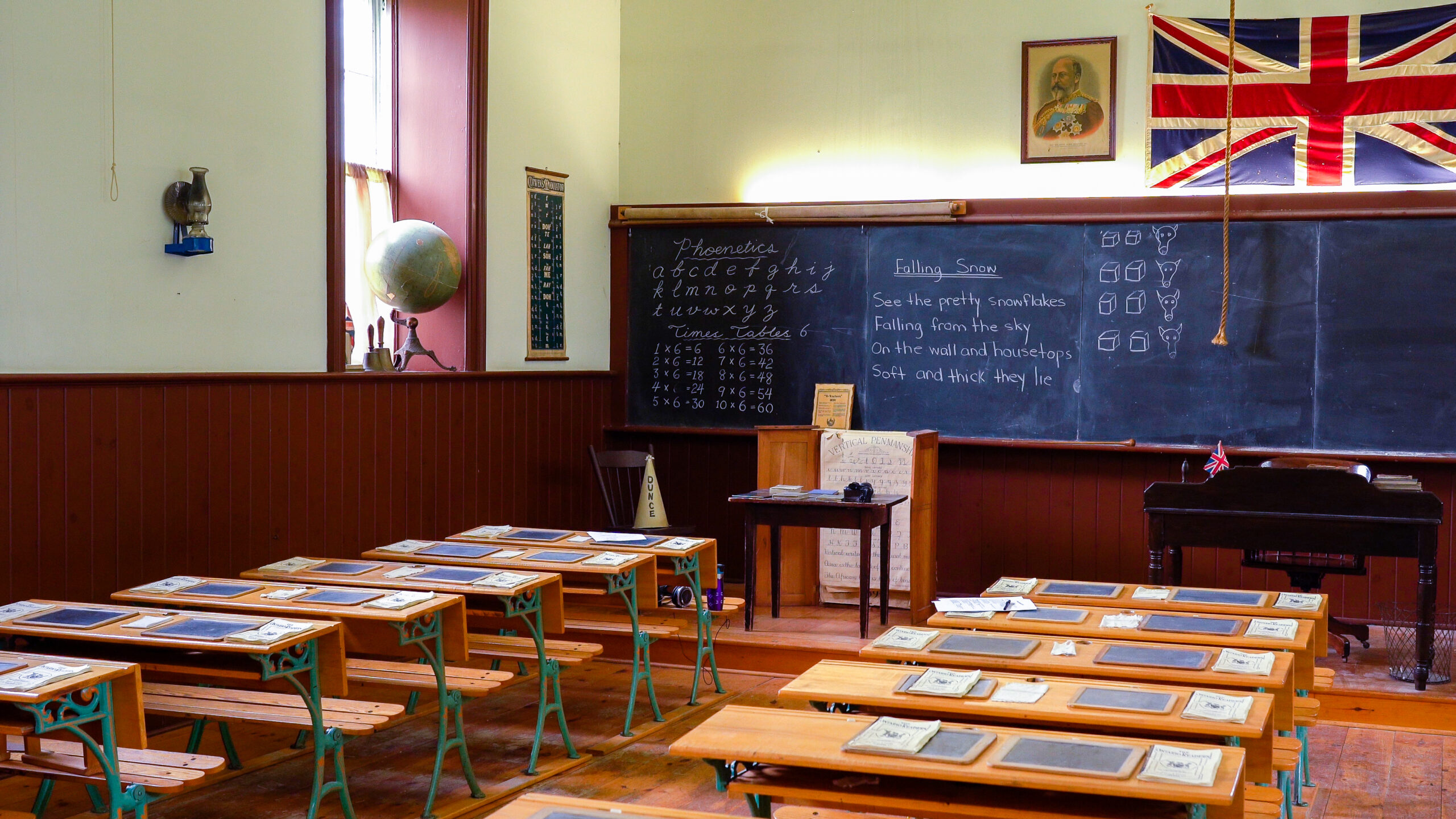 An old school room with wooden desks and the British flag above a chalk board